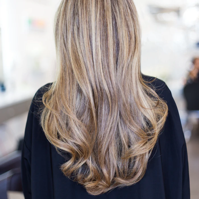 Dopo: capelli lunghi, morbidi e luminosi con schiariture bionde e riflessi caldi, visti di spalle
