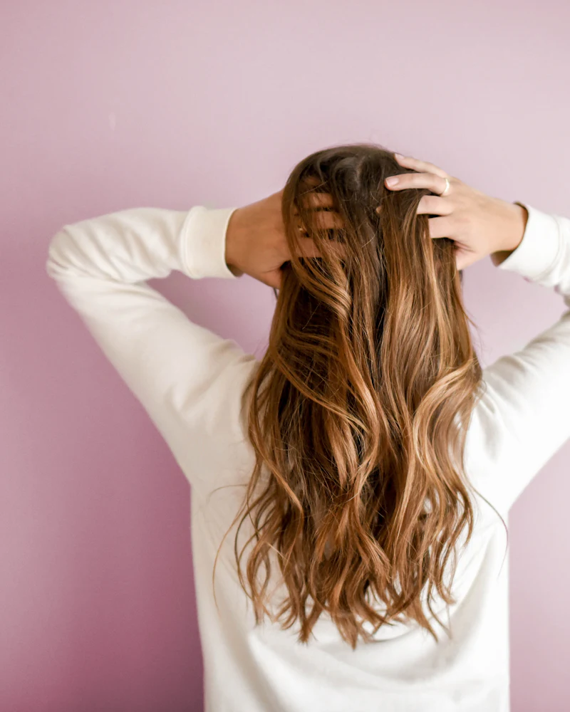 Una donna di spalle con lunghi capelli castani mossi e schiariture color miele